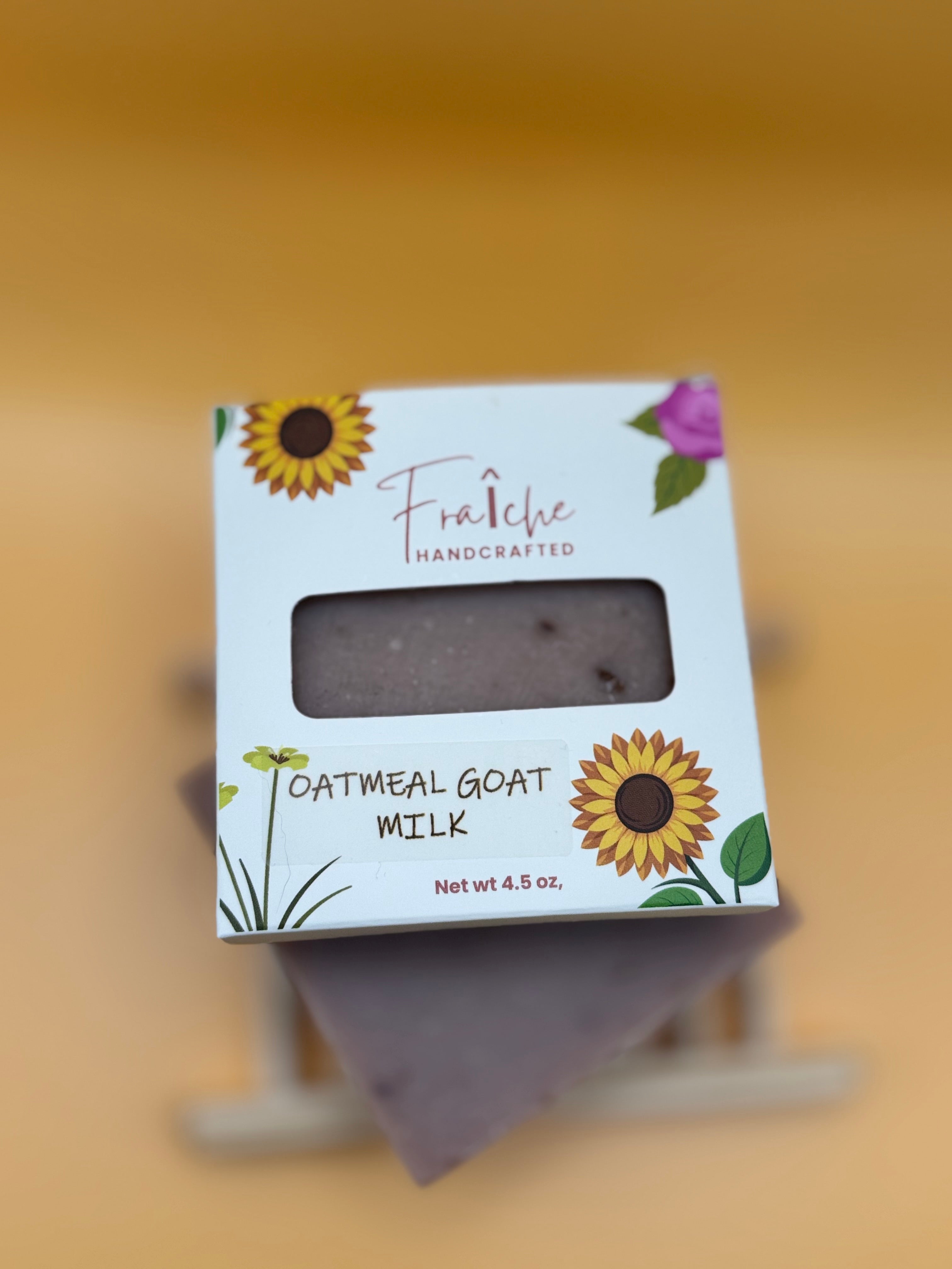 Oatmeal goat milk soap with a white packaging label featuring sunflowers and greenery on a beige background.